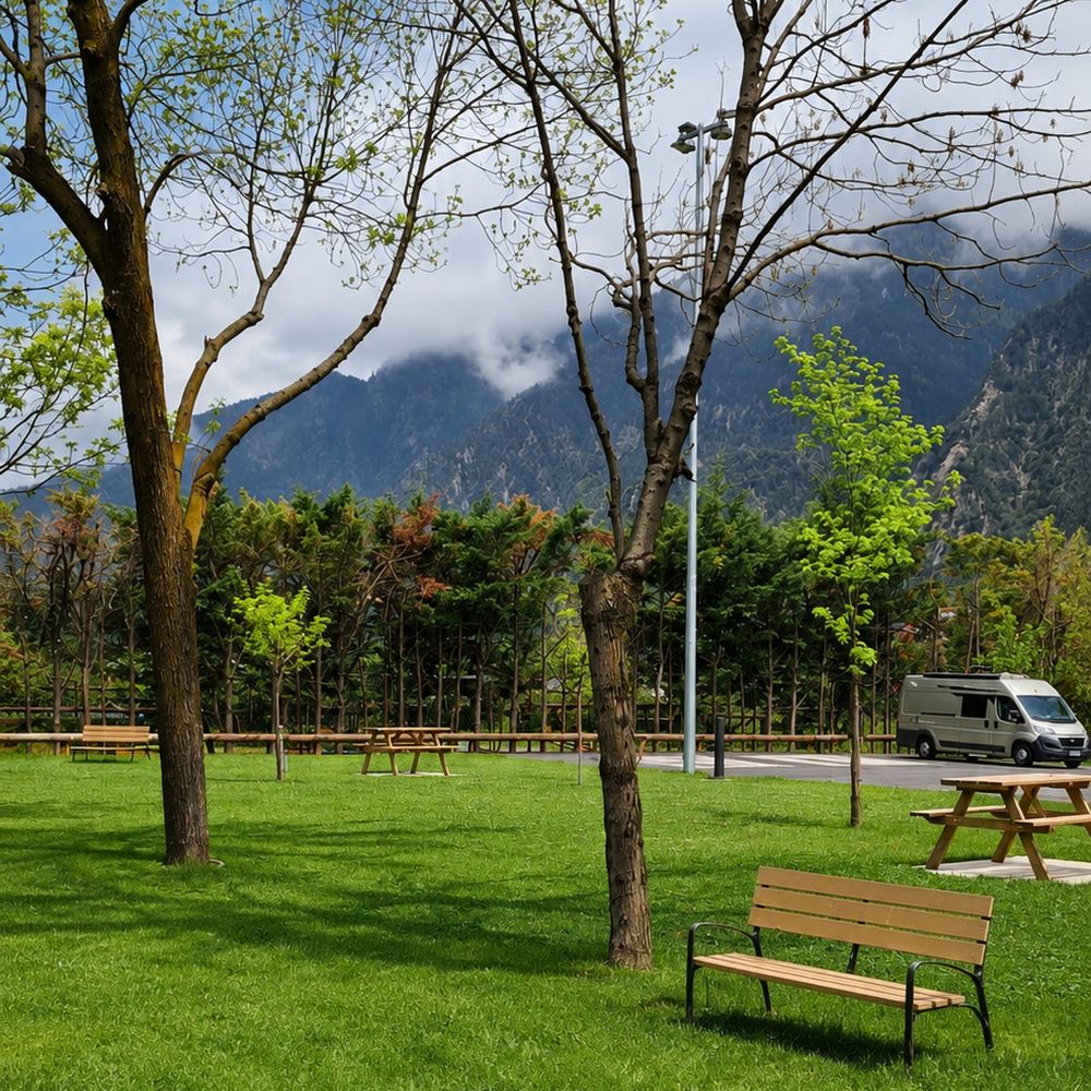 Zona verda amb bancs i autocaravana a l'àrea Canrodes, envoltada de muntanyes